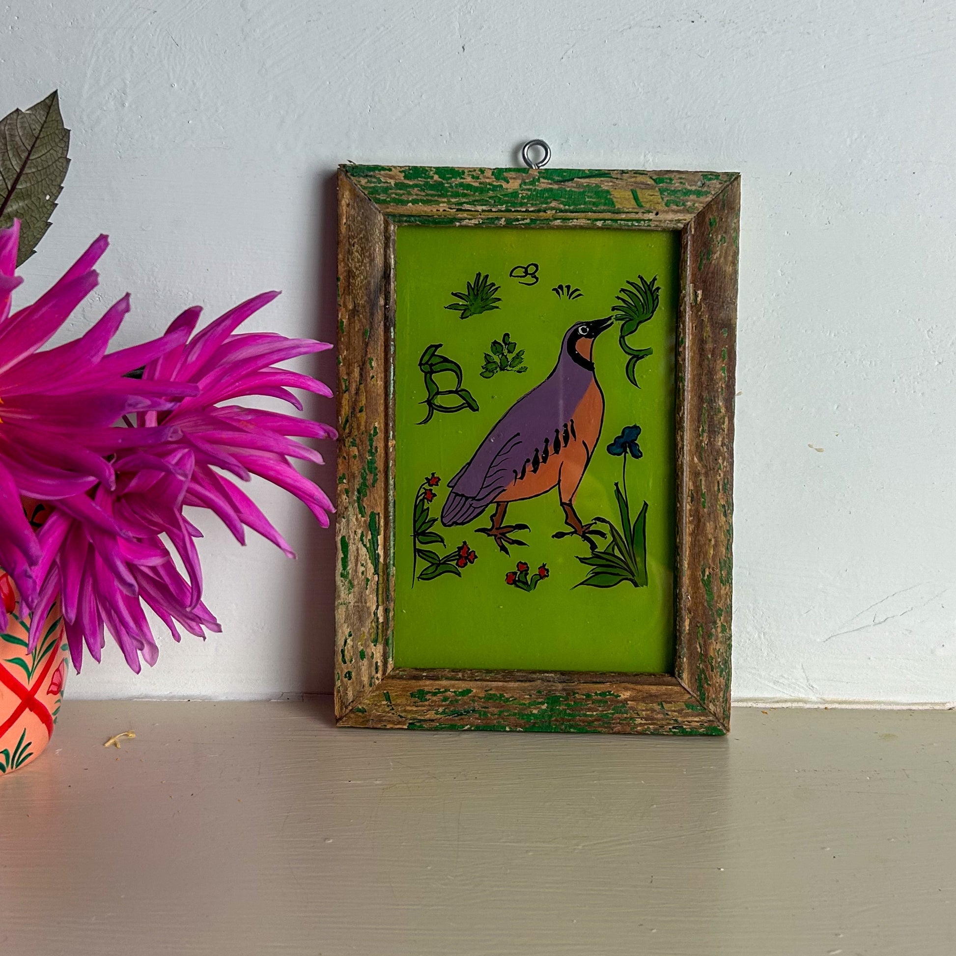 Framed artwork of a bird on a green background with a pink flower in the foreground.