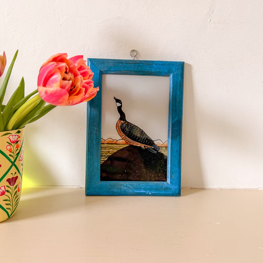 Framed artwork of a peacock with a vase of flowers on a table