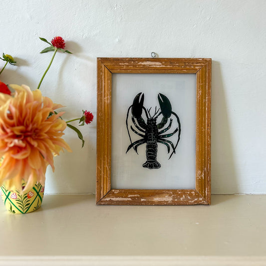 Framed artwork of a black lobster on a white background with a vase of flowers to the left. constance-and-denny-indian-reverse-glass-painting-boxed-packaging-hand-painted-artisan-art-lobster