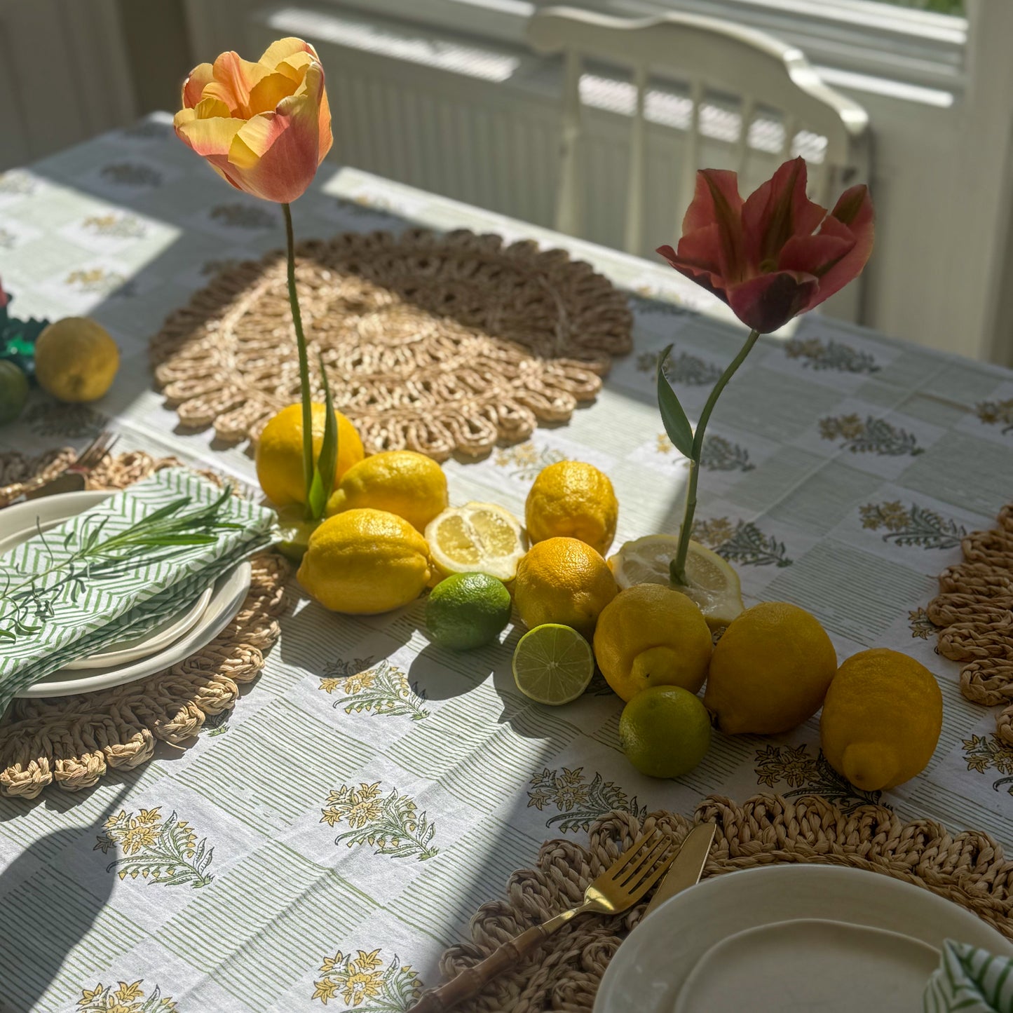 Table setting with lemons, limes, and tulips on a floral tablecloth.