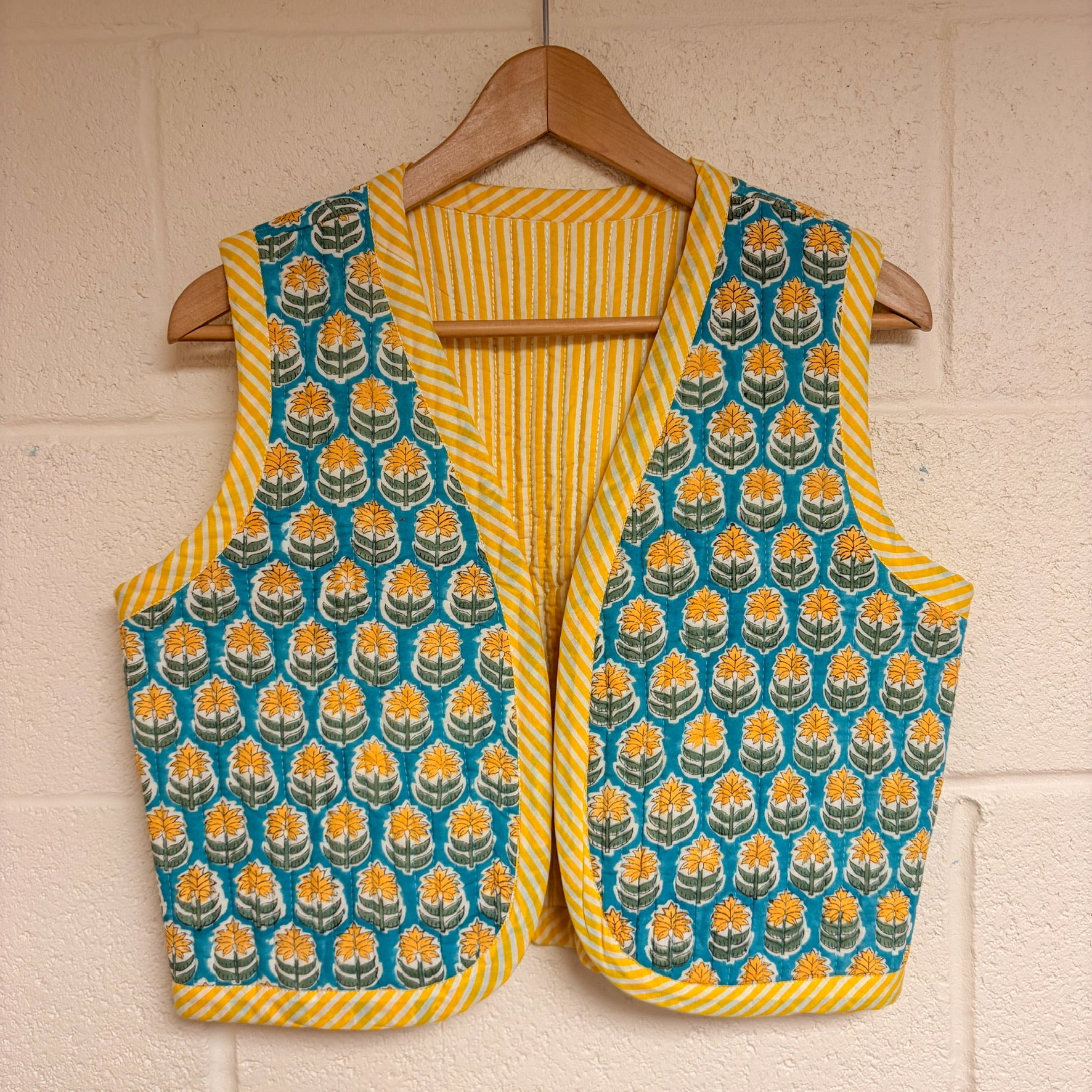 Yellow and blue patterned vest on a hanger against a white brick wall.