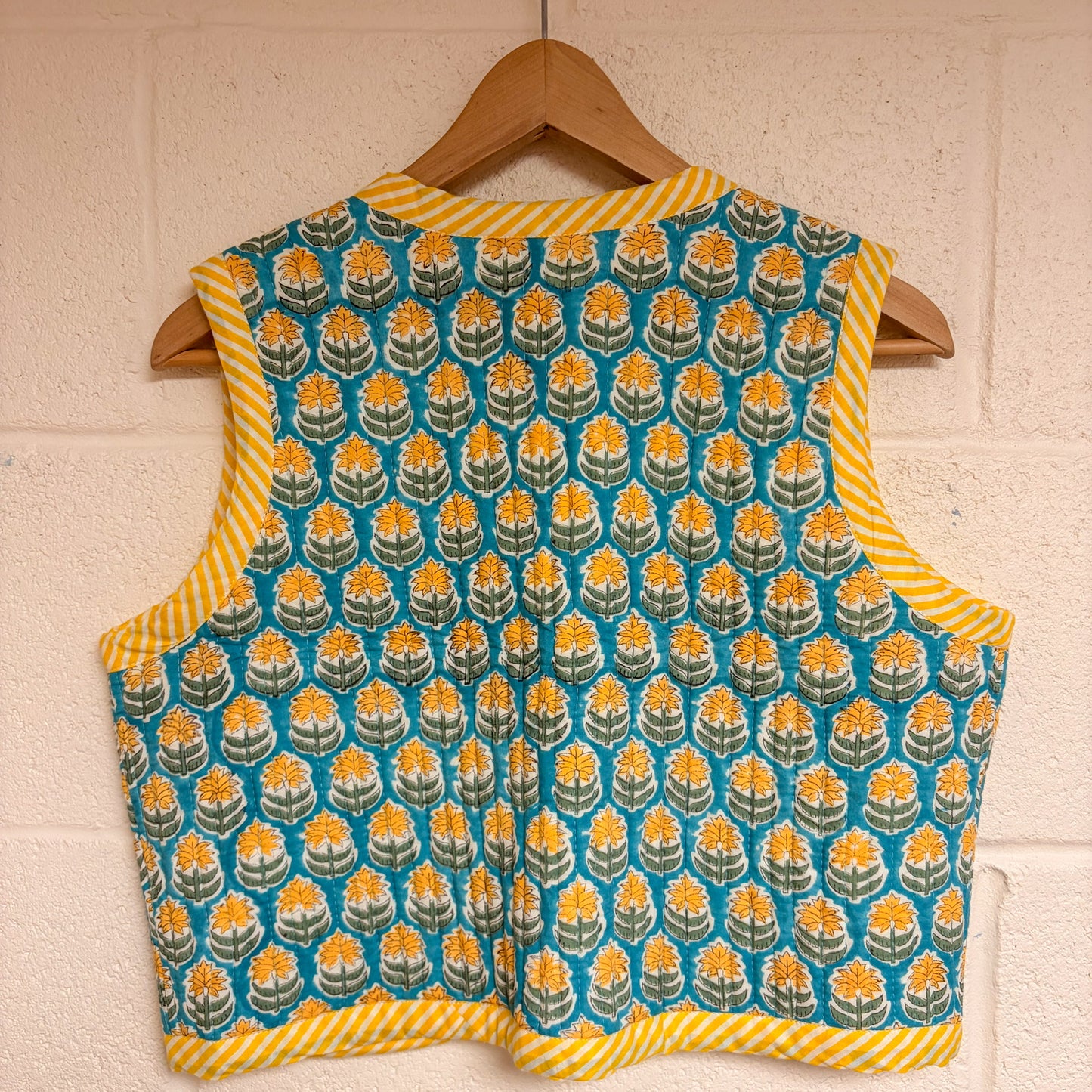 Patterned sleeveless top on a wooden hanger against a white brick wall.