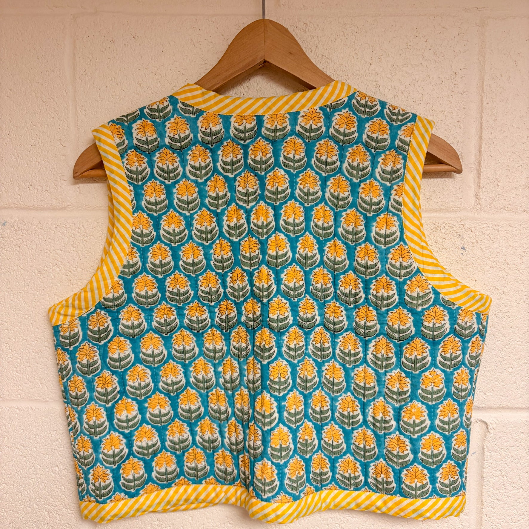 Patterned sleeveless top on a wooden hanger against a white brick wall.