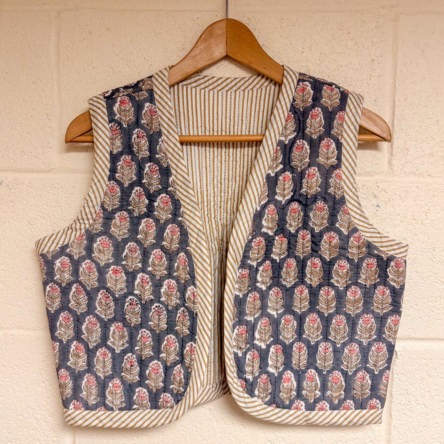 waistcoat hanging on a wooden hanger against a beige wall.