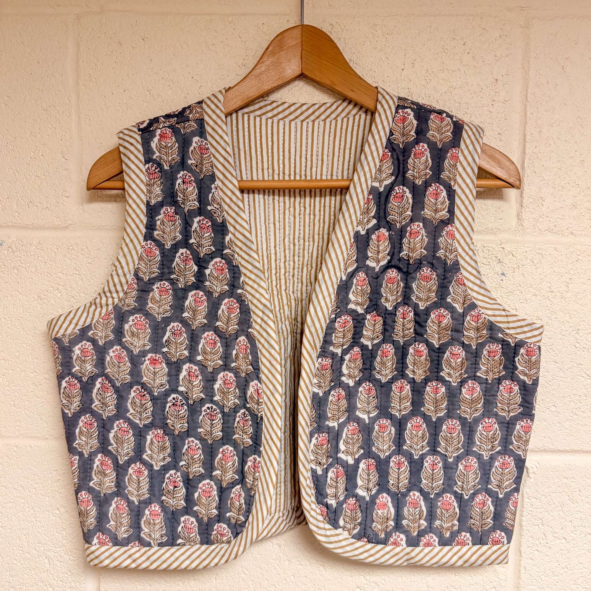 waistcoat hanging on a wooden hanger against a beige wall.