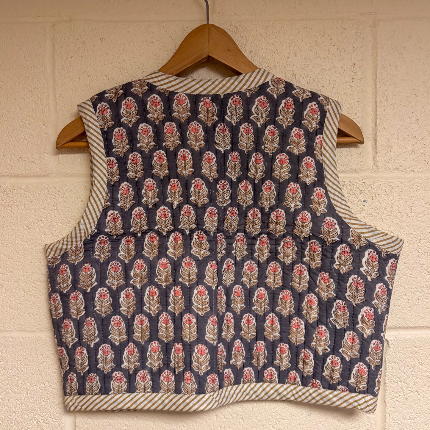 Patterned waistcoat on a wooden hanger against a textured wall.