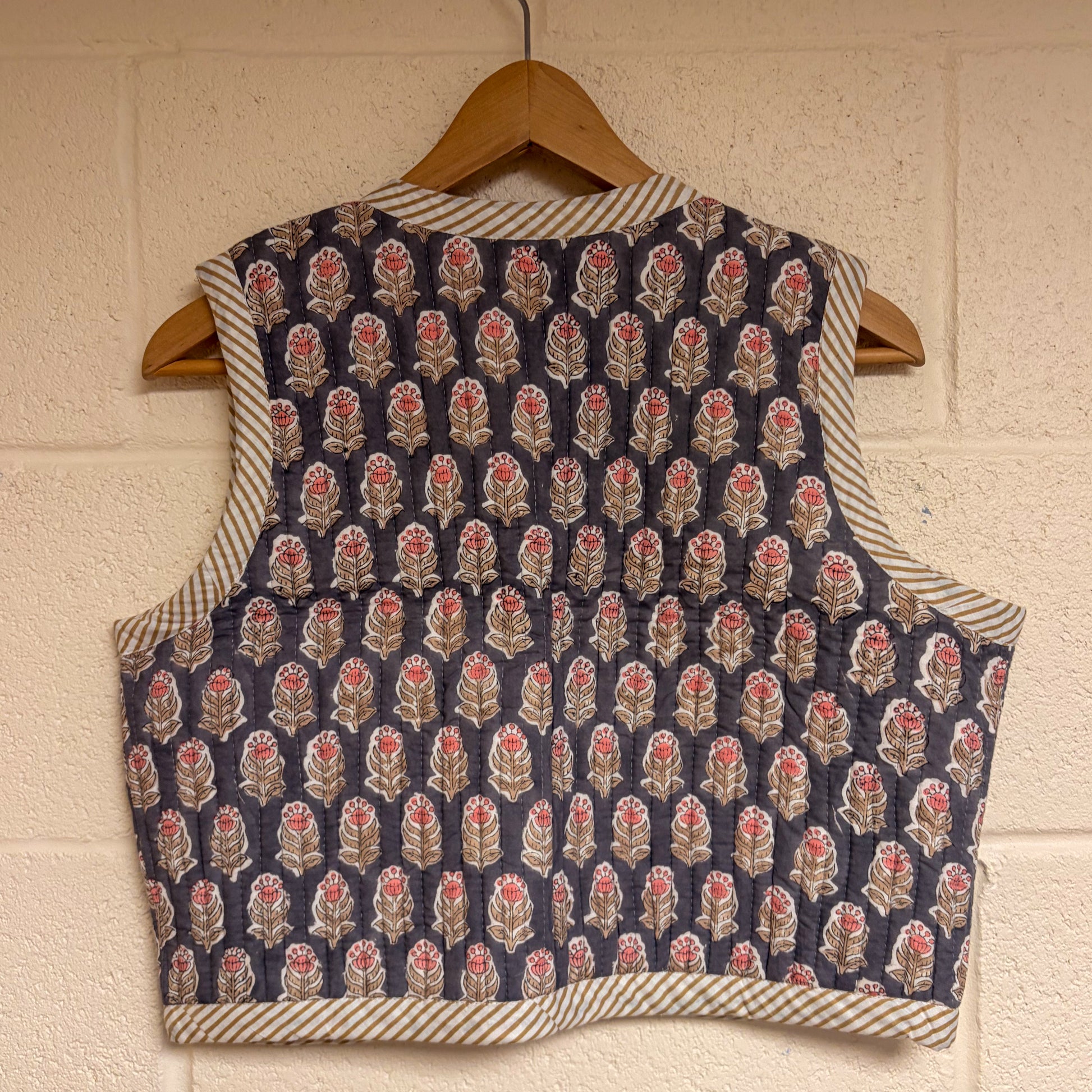Patterned waistcoat on a wooden hanger against a textured wall.