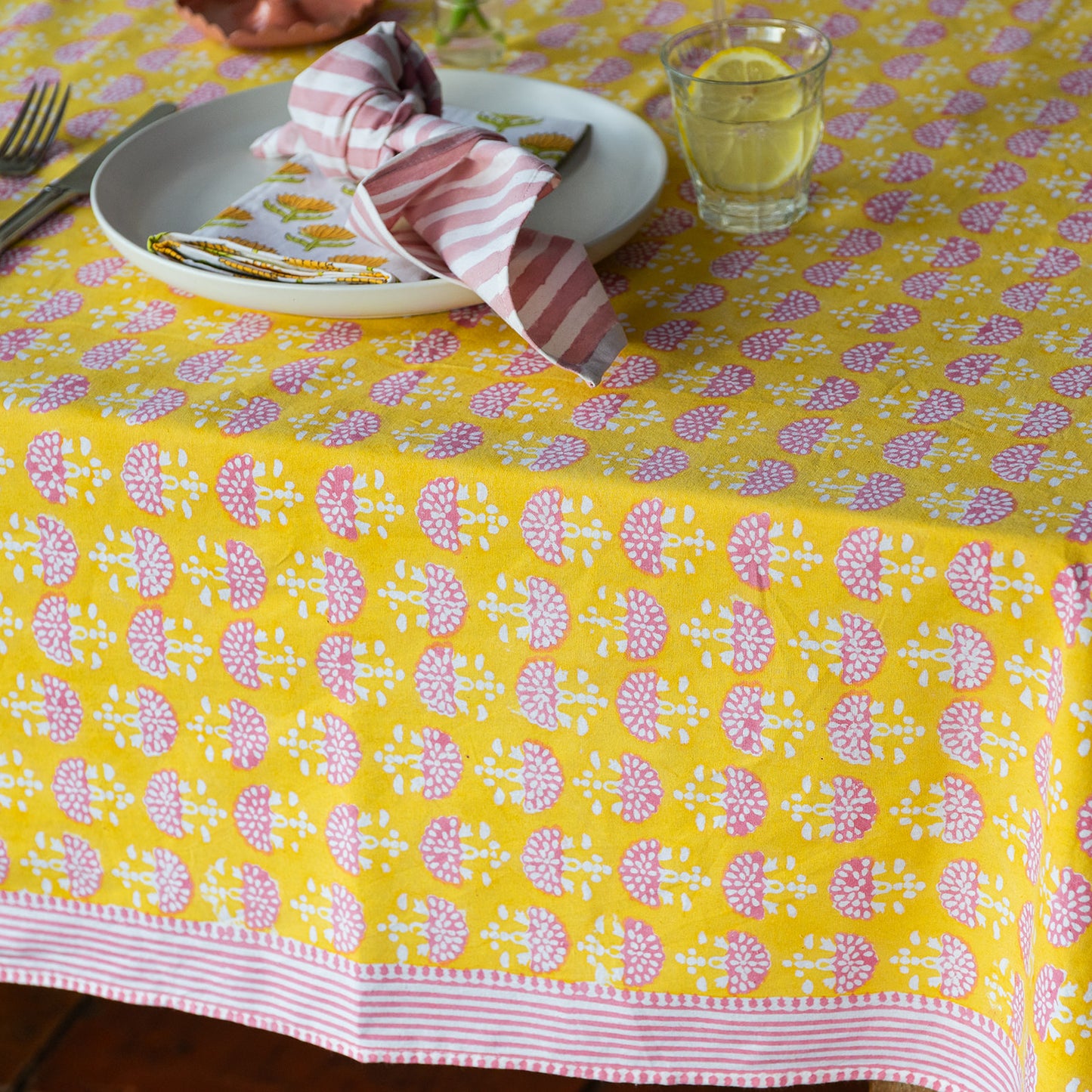 Yellow tablecloth with pink floral pattern on a set dining table.