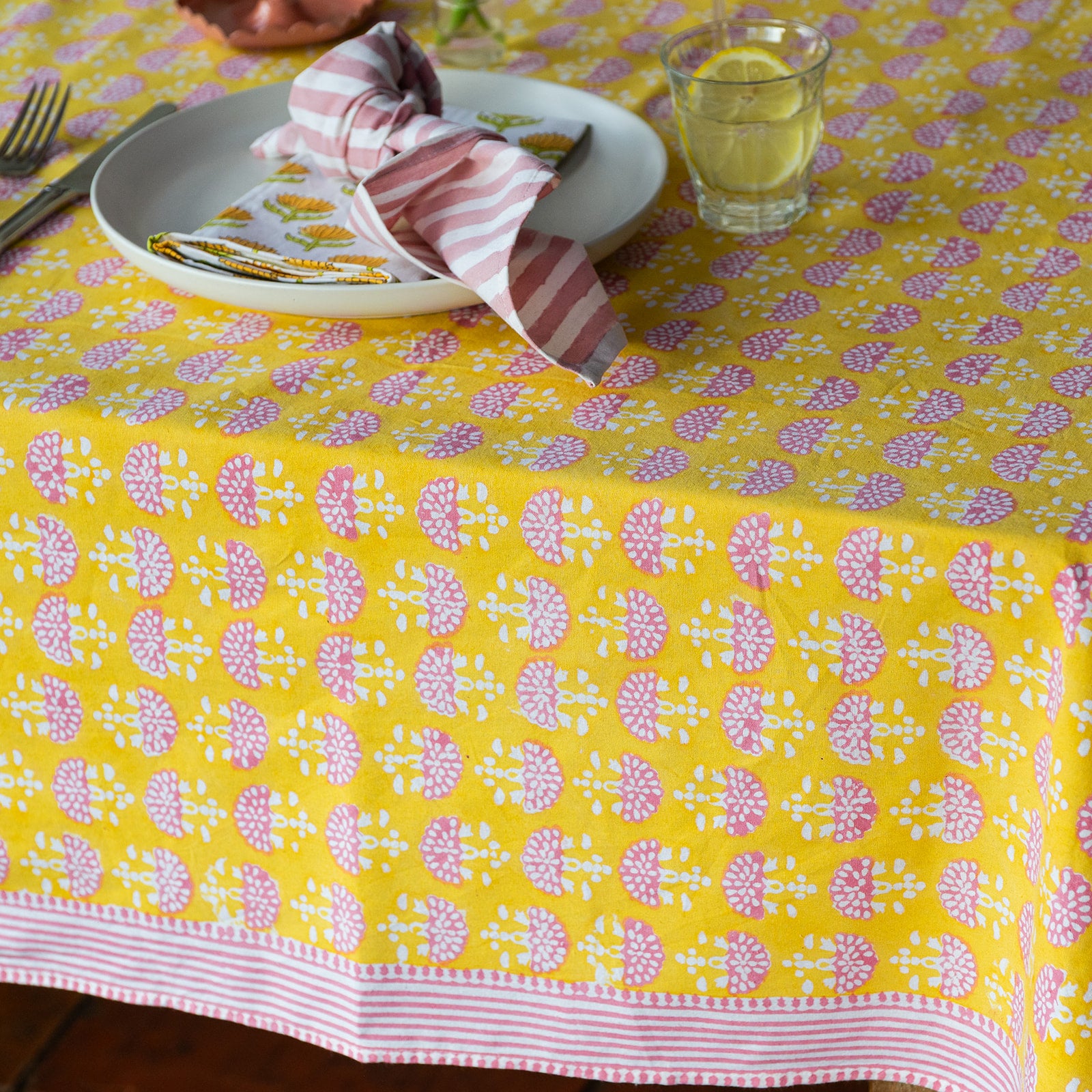 Yellow tablecloth with pink floral pattern on a set dining table.