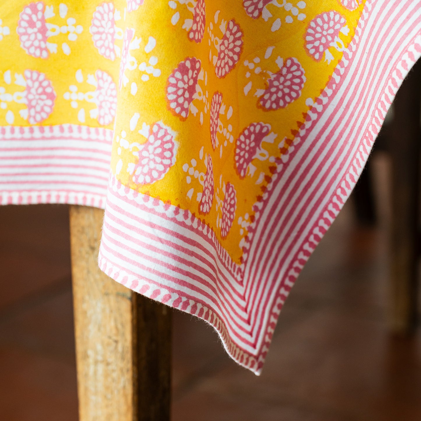Close-up of a yellow and pink patterned tablecloth draped over a wooden chair.