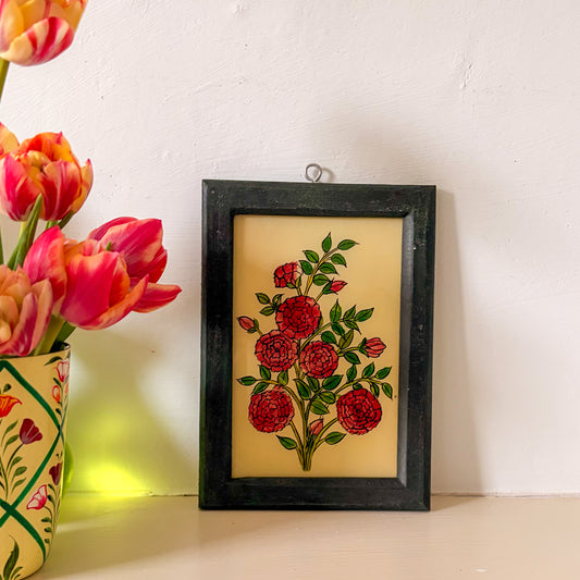 Framed floral artwork with red flowers on a white wall next to a vase of pink and orange tulips.