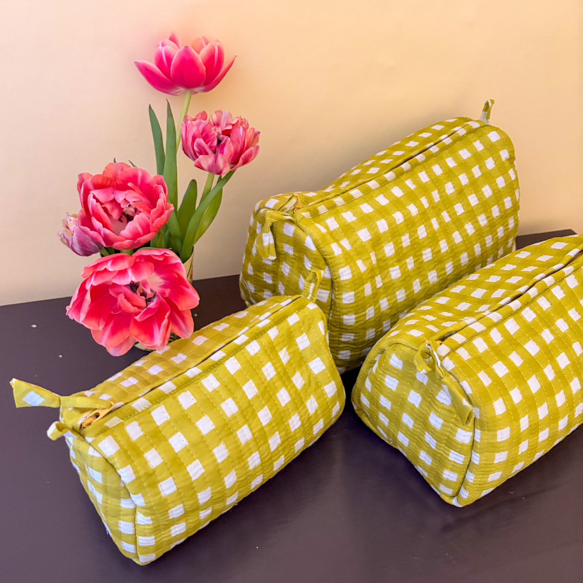Three alchemilla checkered bags on a dark surface with pink tulips in the background.