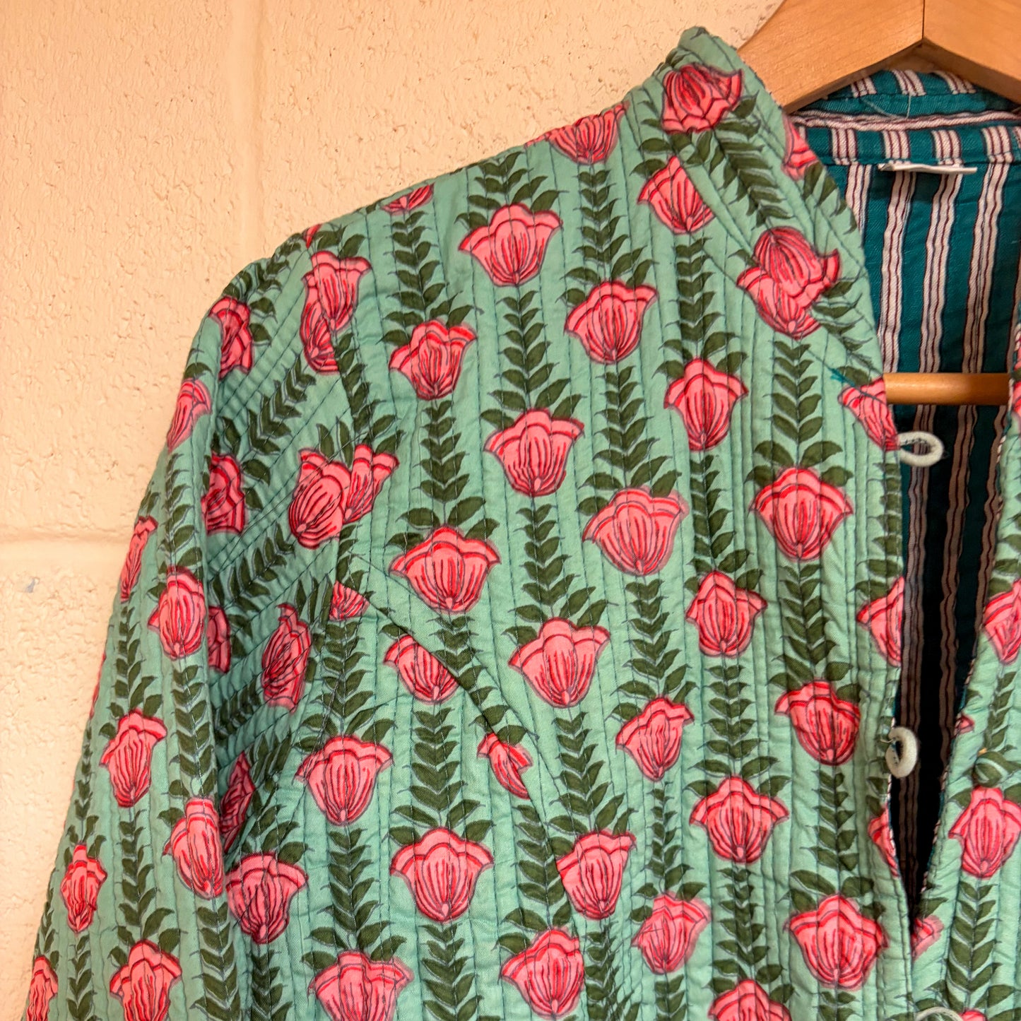 Green fabric with red floral pattern on a wooden hanger against a beige wall.