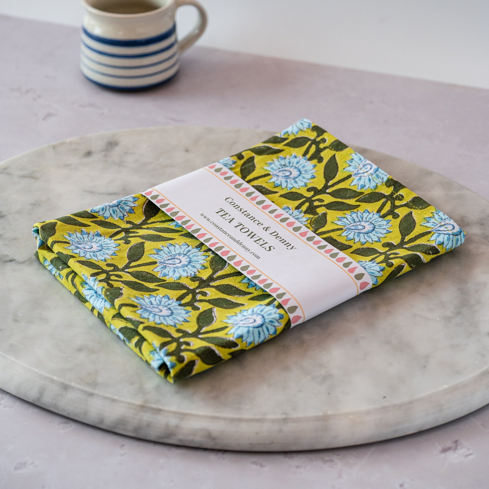 Packaged floral tea towel on a marble surface with a mug in the background