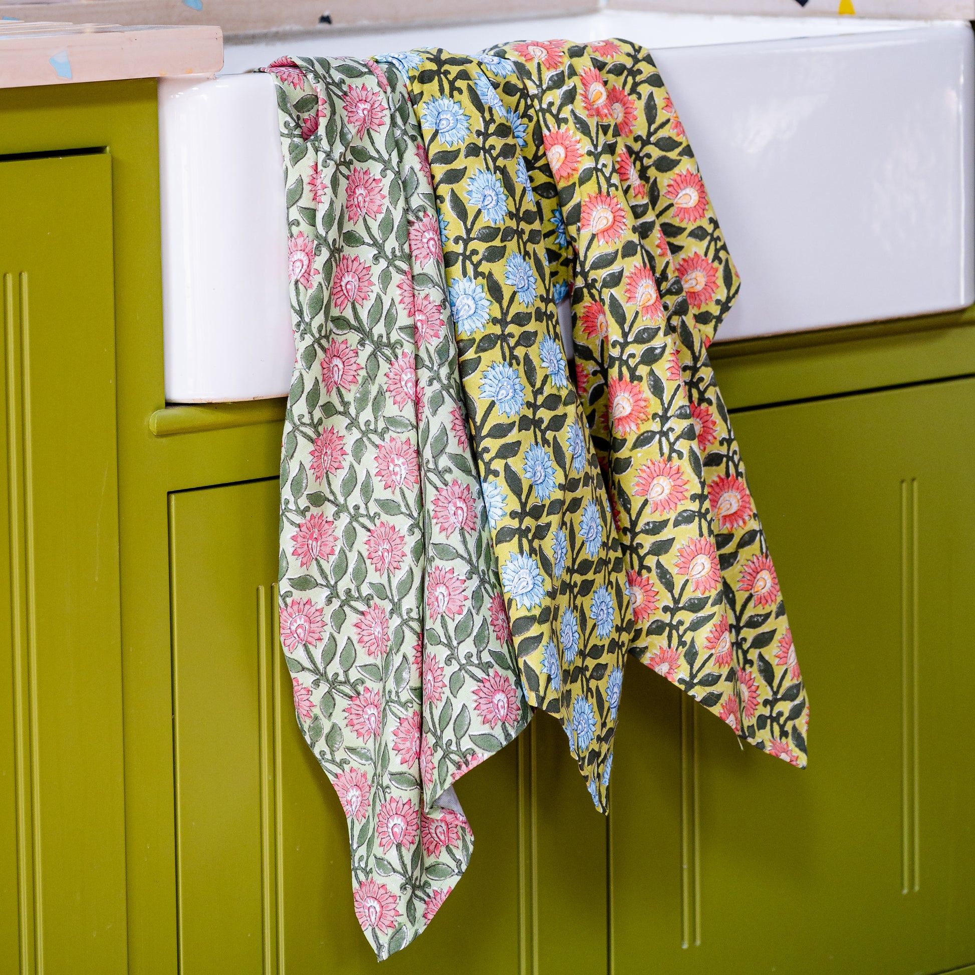 Floral-patterned tea towels hanging on a green cabinet.