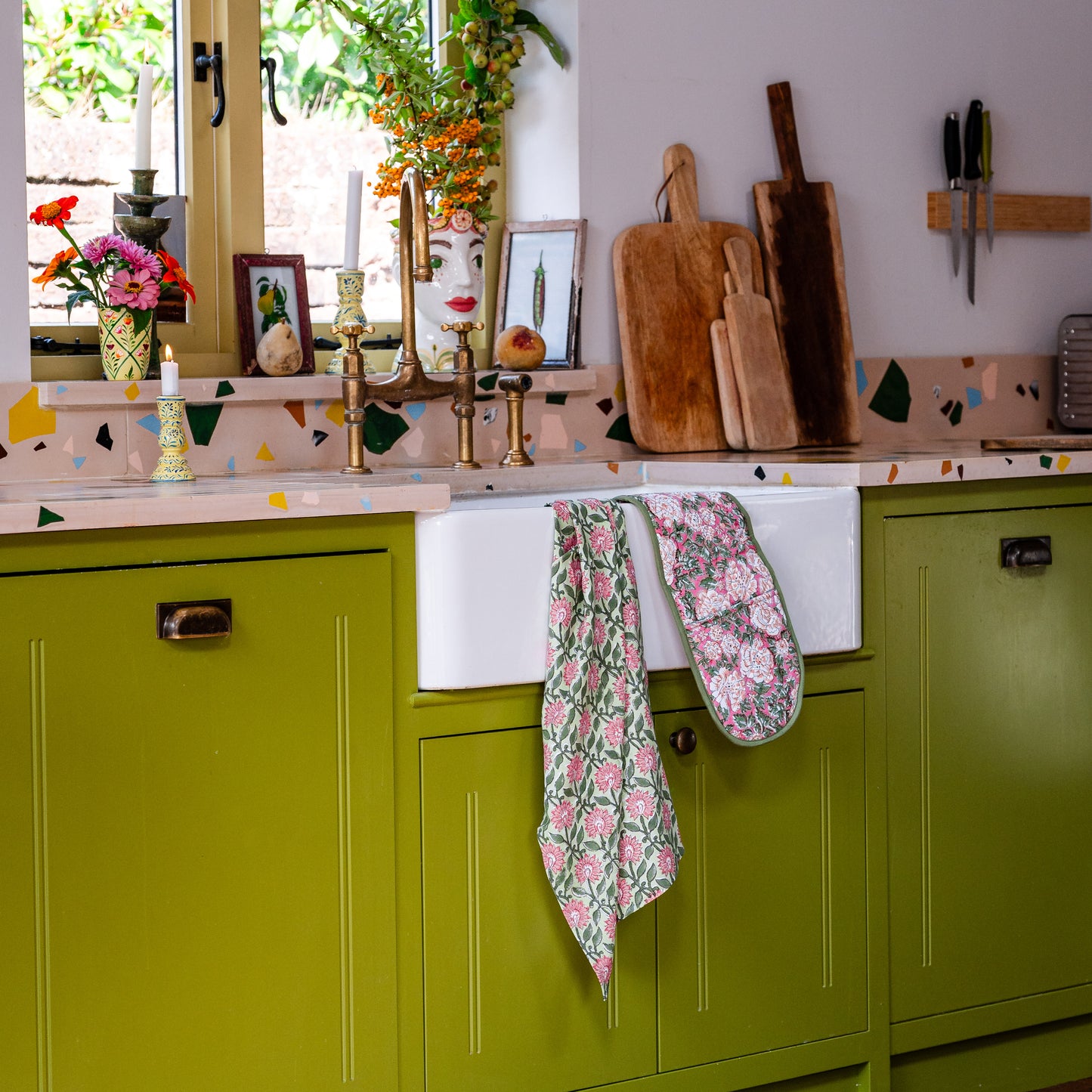 Kitchen with green cabinets, white sink, and floral towels hanging.