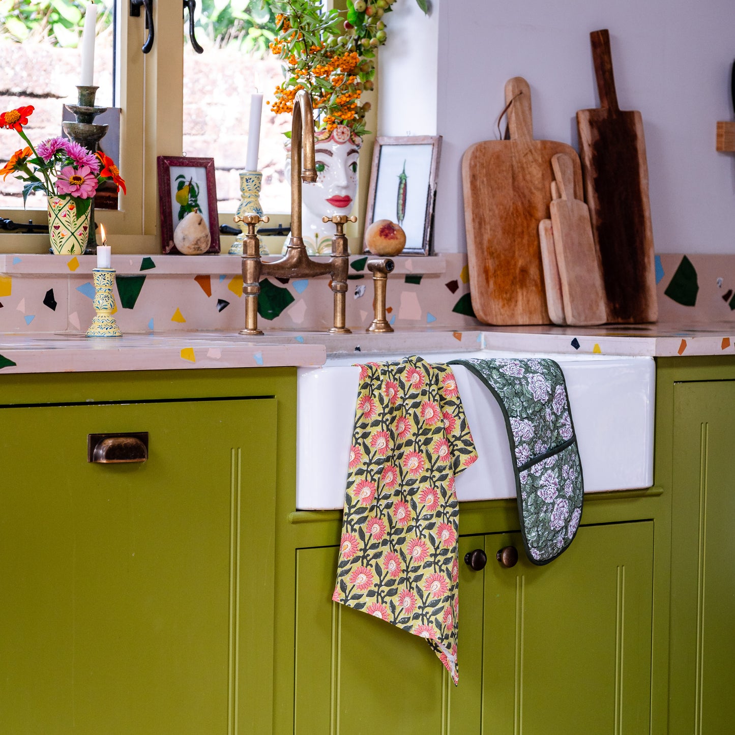 Kitchen with green cabinets, white sink, and floral towels hanging on the handle.