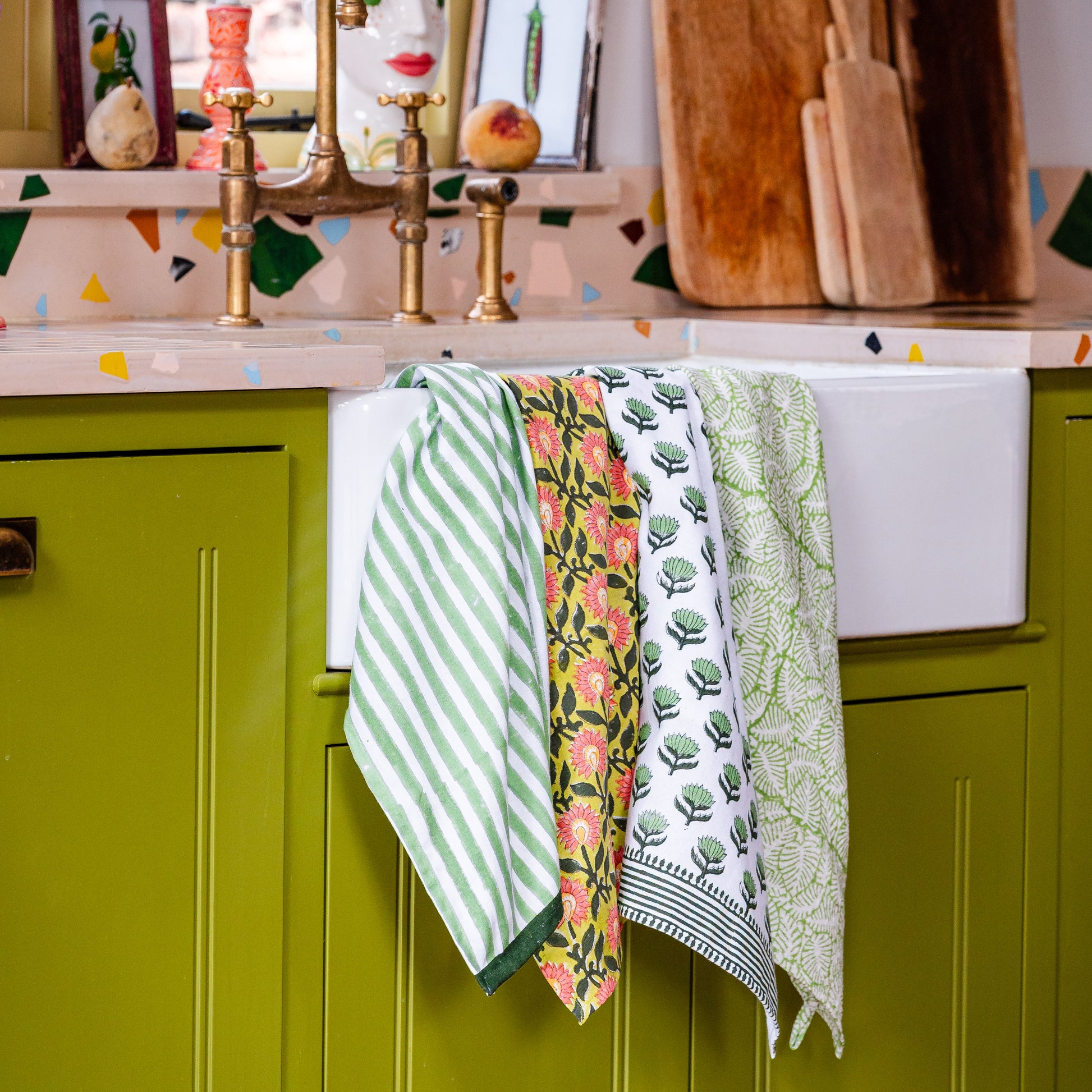 Colorful kitchen scene with green cabinets, floral towels, and a sink.