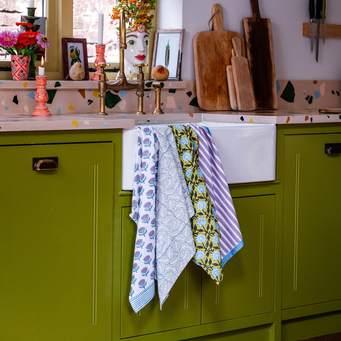 Colorful kitchen scene with green cabinets, patterned tea towels, and decorative items.