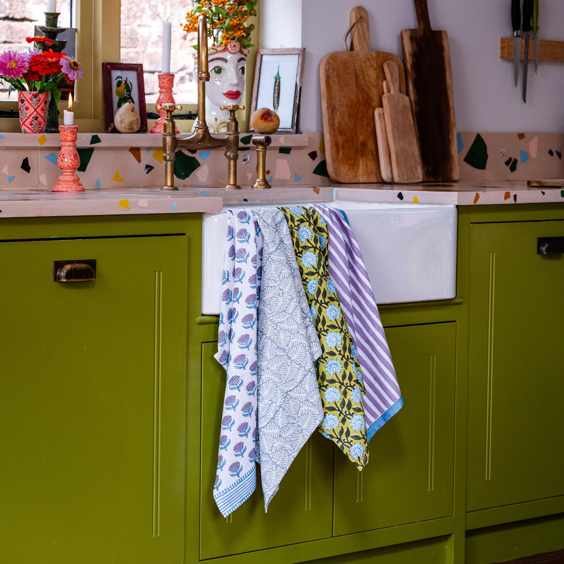 Colorful kitchen scene with green cabinets, patterned tea towels, and decorative items.