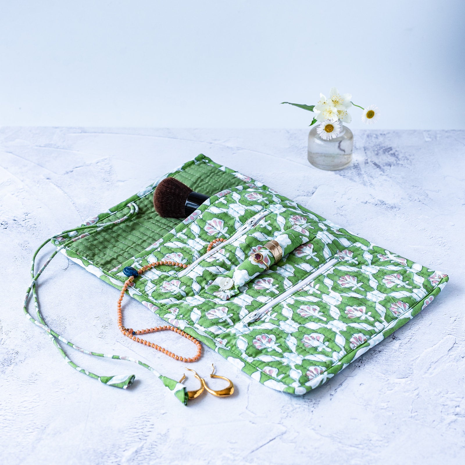 Green floral makeup roll-up organizer with accessories on a light surface. JEWELLERY-ROLL-PETAL-BLOCK-PRINTED