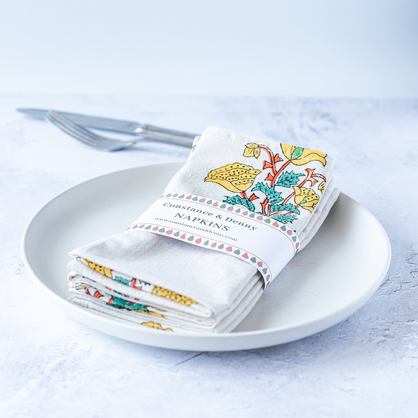 Set of folded napkins with floral design on a white plate against a light background. FLORAL-GREEN-YELLOW-FLOWER