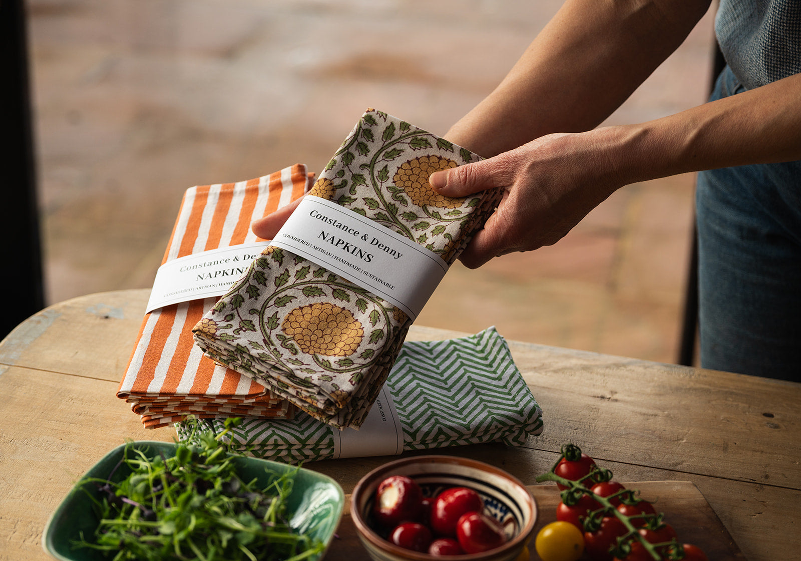 Person holding a pack of patterned napkins on a wooden table with food items.