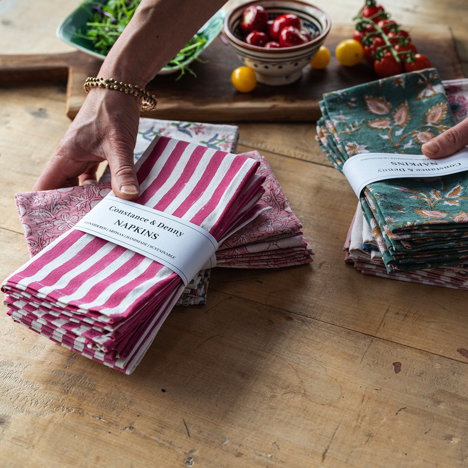 Bundles of patterned napkins on a wooden table with food items in the background.