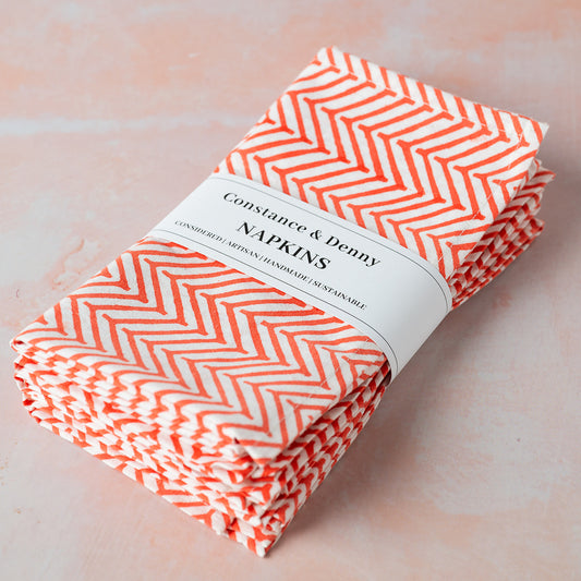 Pack of Constance & Penny napkins with orange chevron pattern on a light pink background