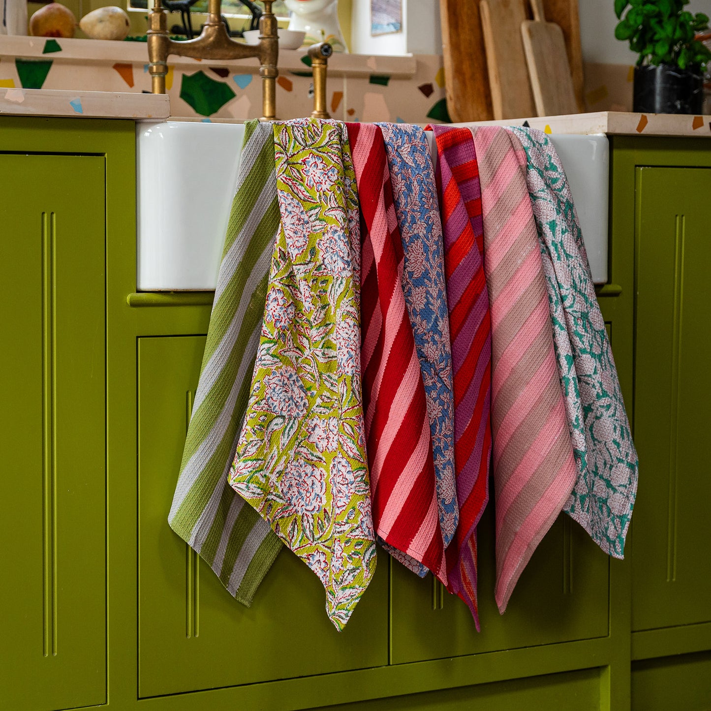 Colorful patterned towels hanging on a towel rack against a green kitchen cabinet.