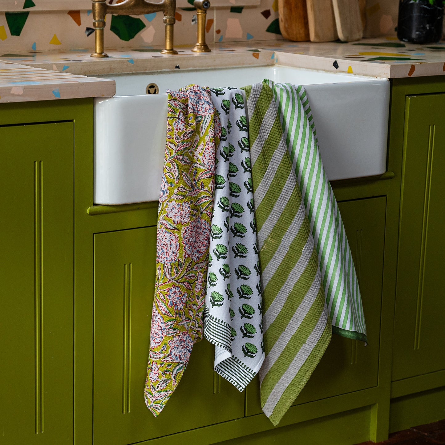 Colorful kitchen towels hanging over a white sink in a green kitchen.