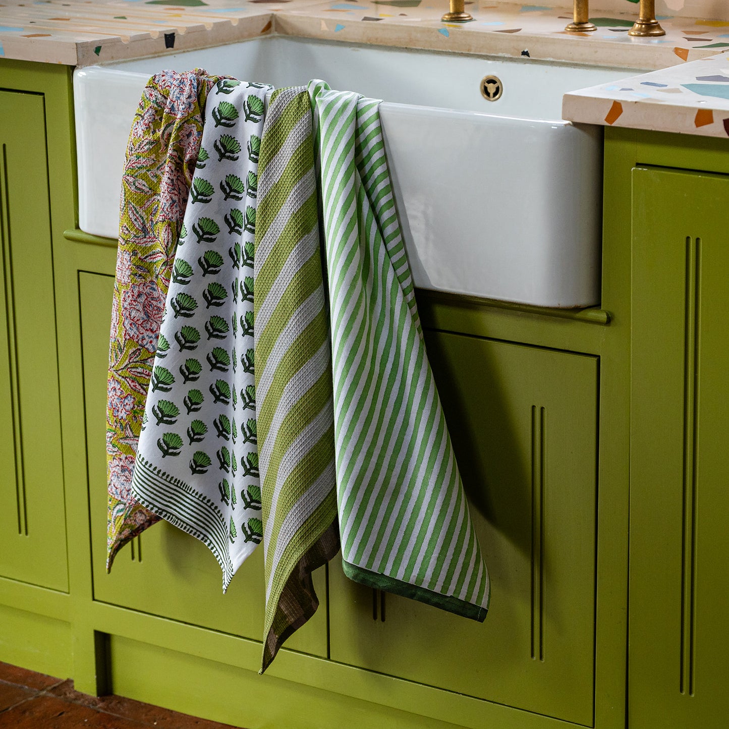 Green kitchen cabinet with a white sink and colorful towels hanging on the side.