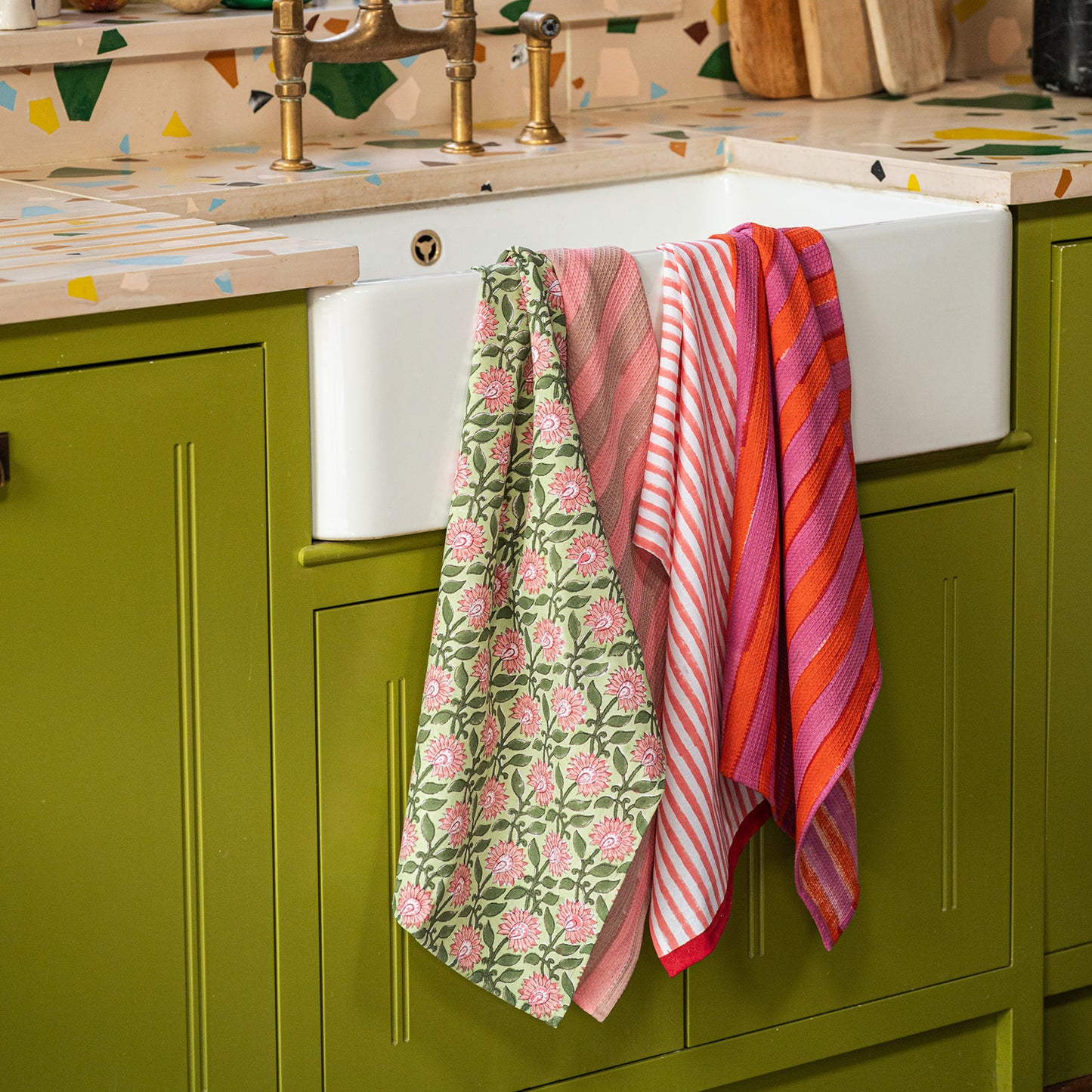 Colorful kitchen towels hanging on a green cabinet with a sink in the background.
