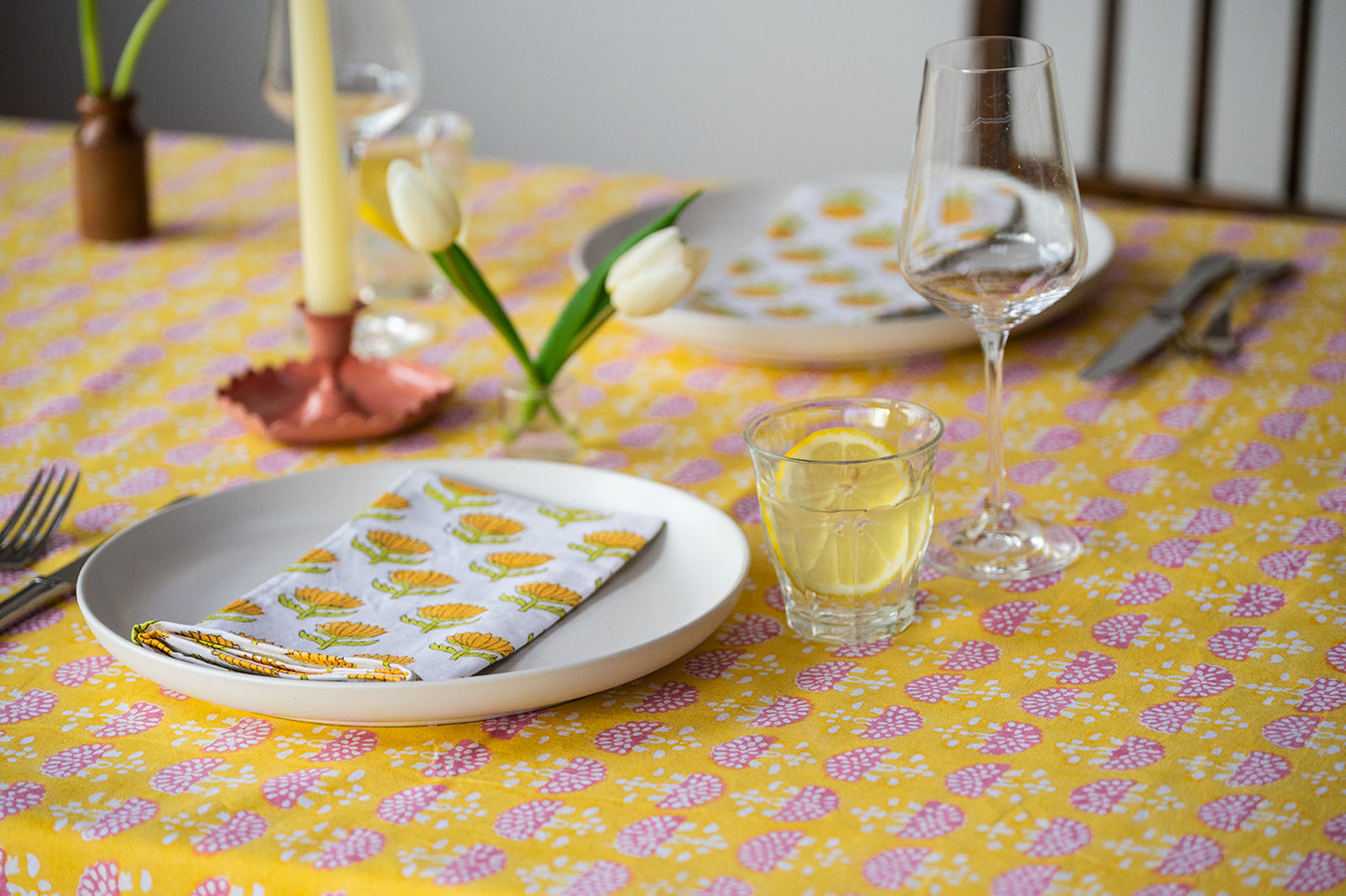 Dining table setting with plates, glasses, and cutlery on a yellow floral tablecloth.
