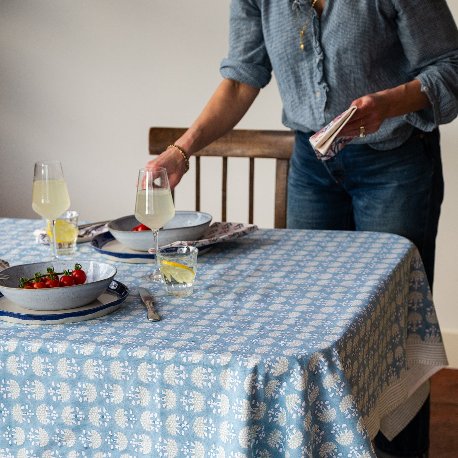 Person setting a table with a blue and white checkered tablecloth, glasses of lemonade, and plates.