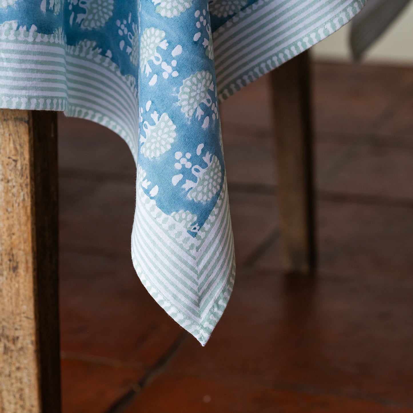 Blue and white patterned tablecloth draped over a wooden chair on a wooden floor.