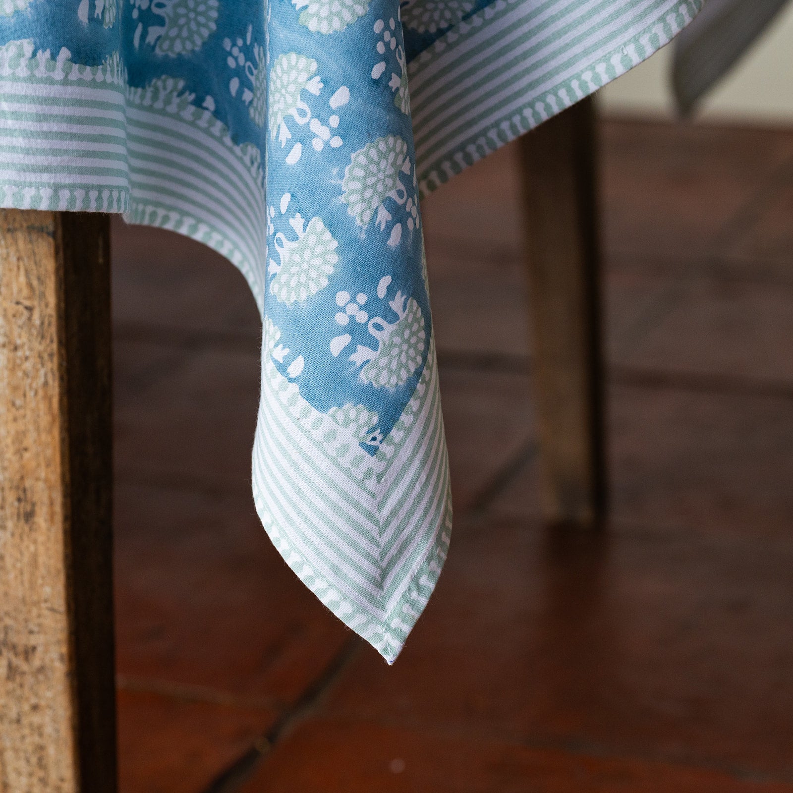 Blue and white patterned tablecloth draped over a wooden chair on a wooden floor.