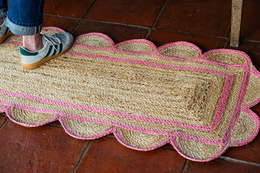 Scalloped jute rug with pink trim on a tiled floor