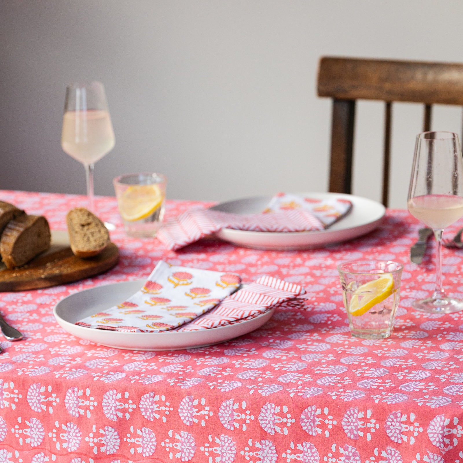Dining table setting with plates, glasses, and a pink floral tablecloth.