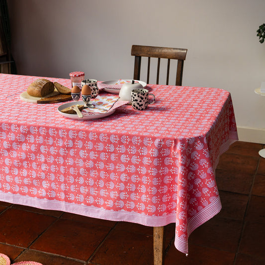Table with a pink and white patterned tablecloth, food items, and a chair.