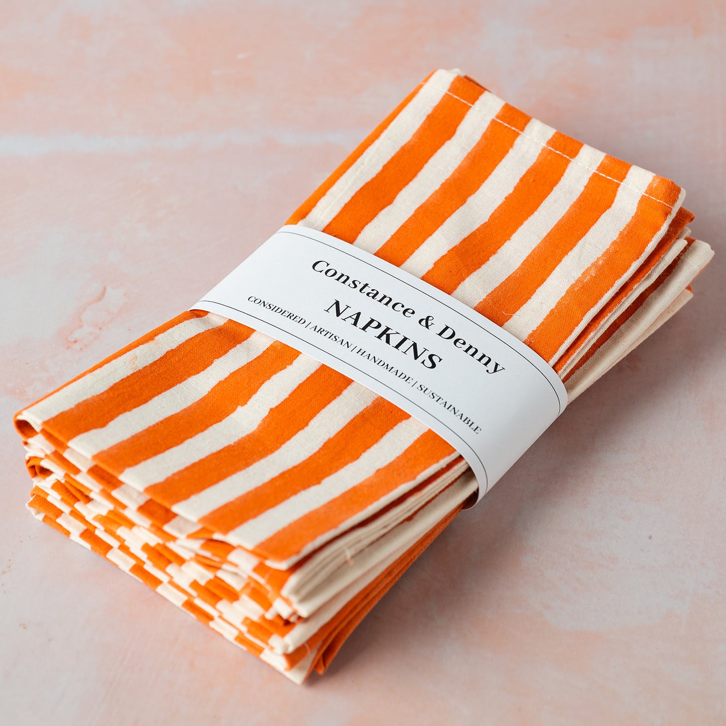 Stack of orange and white striped napkins with a label on a light pink background
