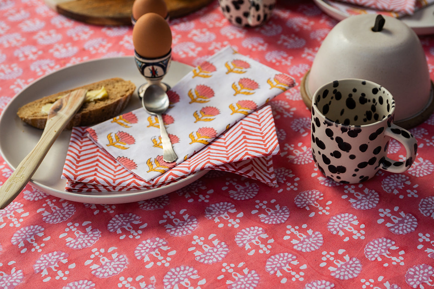 Breakfast setting with toast, eggs, and a cup on a red floral tablecloth.