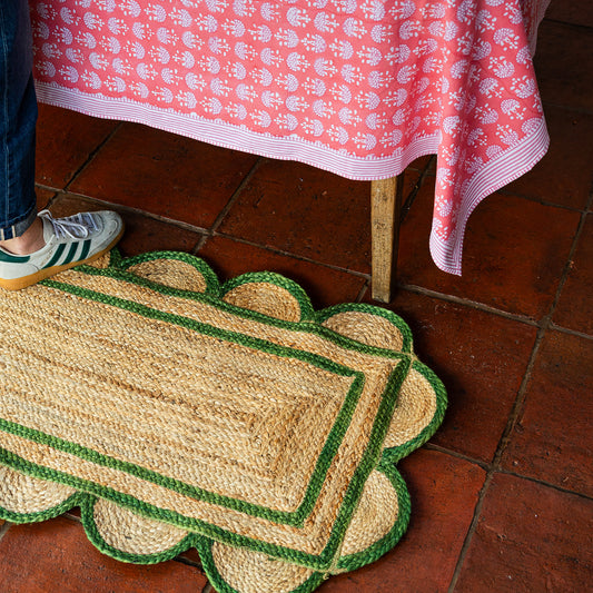 Scalloped edge doormat on a tiled floor with a red floral tablecloth in the background.