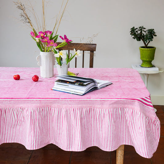 Table with pink and white striped tablecloth, flowers, books, and a plant.