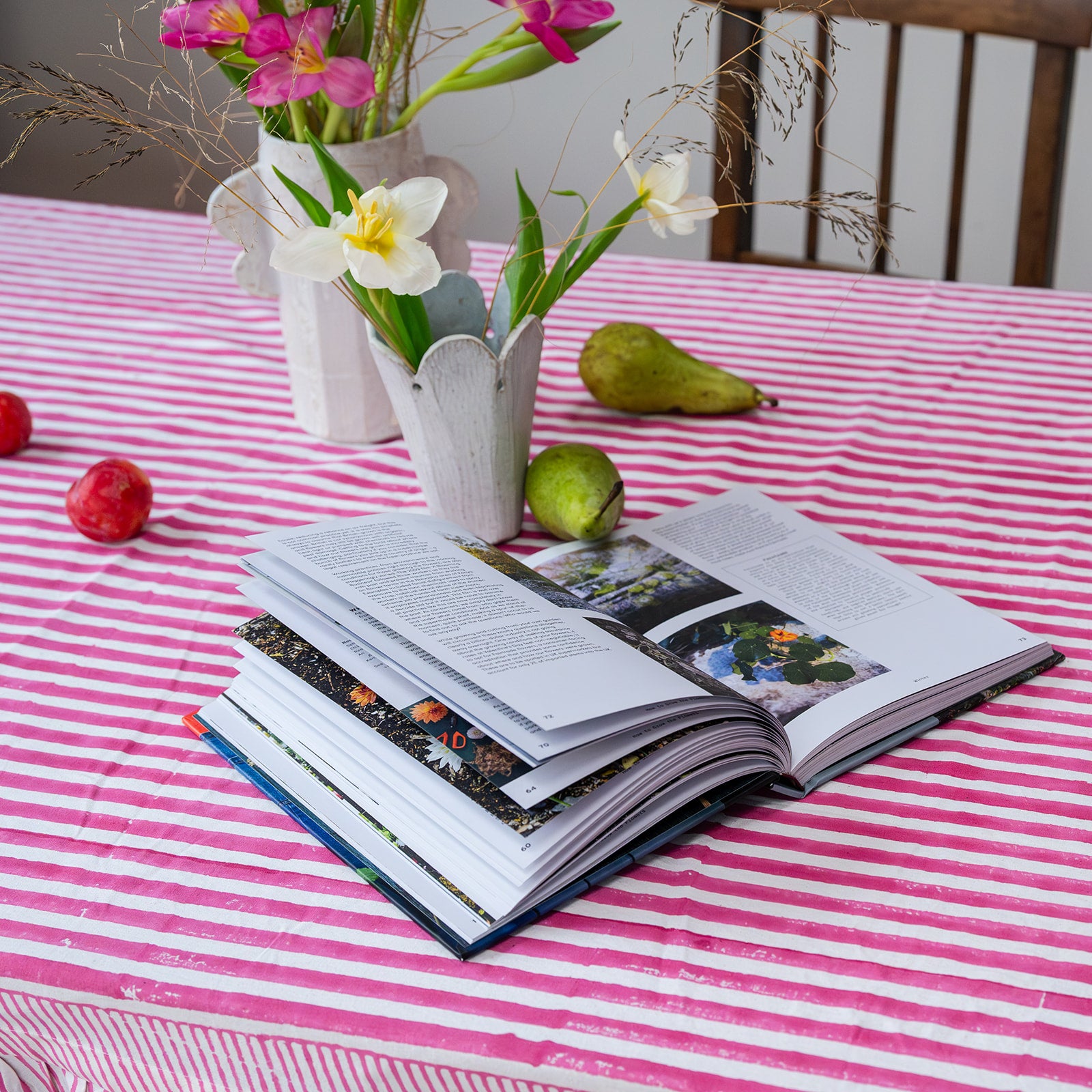 Open book on a pink and white striped tablecloth with flowers and pears.