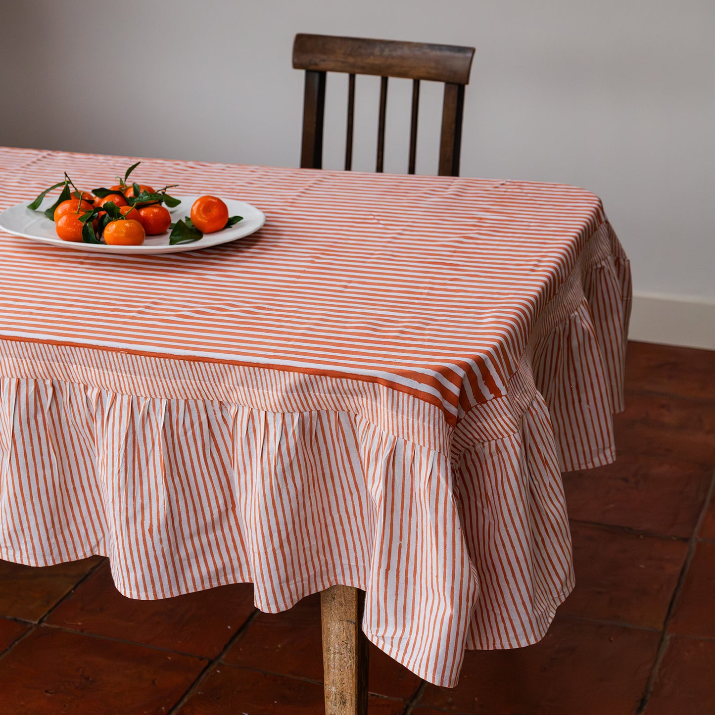 Table with a striped tablecloth, plate of oranges, and chair in a room.