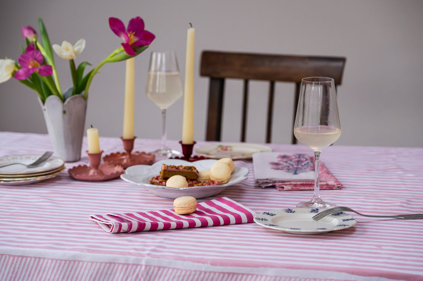Dining table set with plates, glasses, candles, and flowers on a striped tablecloth.