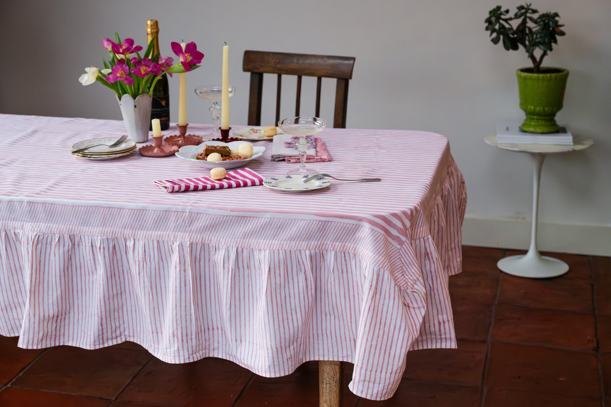 Dining table set with a pink and white checkered tablecloth, plates, and candles in a home setting.
