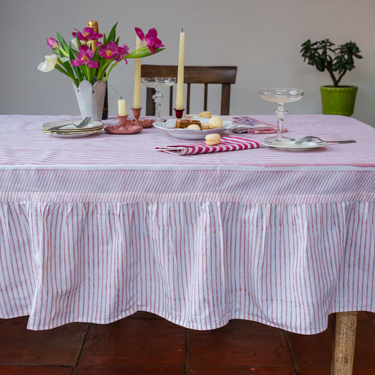 Dining table set with a striped tablecloth, candles, flowers, and cutlery.