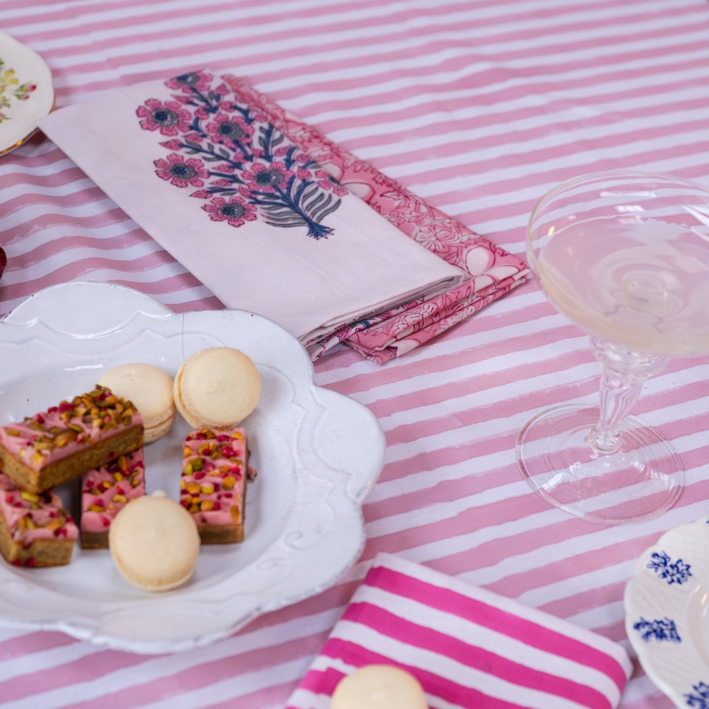 Plate of cookies and macarons on a pink striped tablecloth with a glass of white wine.